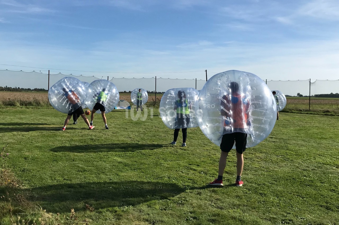 Des personnes jouent au bubble football sur une pelouse, protégées par de grandes bulles gonflables transparentes.