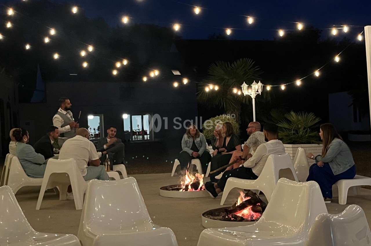 Un groupe de personnes assises autour de braseros allumés, sous des guirlandes lumineuses, en soirée.