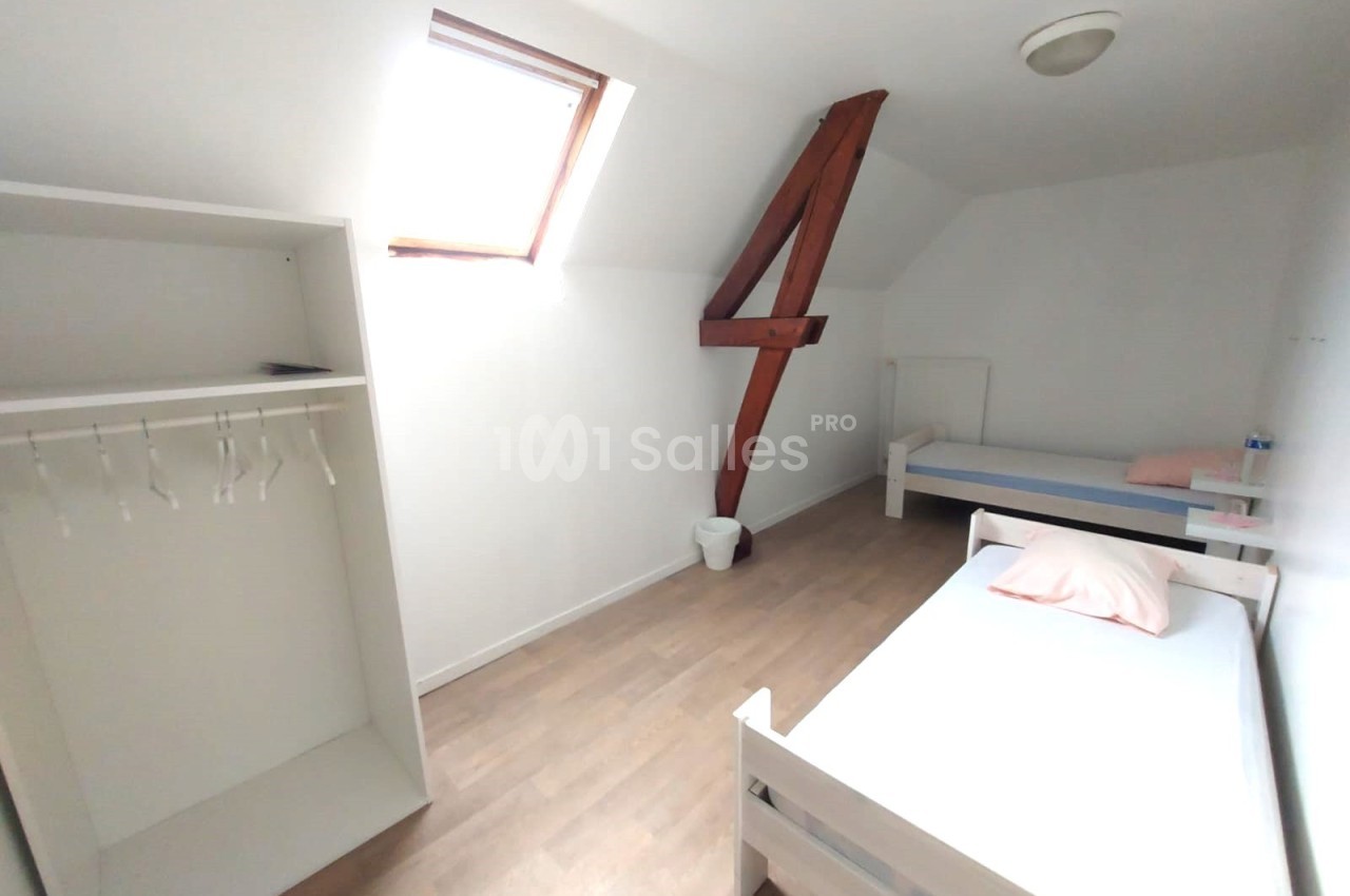 Chambre mansardée avec deux lits simples, un placard ouvert, un mur blanc et une fenêtre de toit apportant de la lumière.