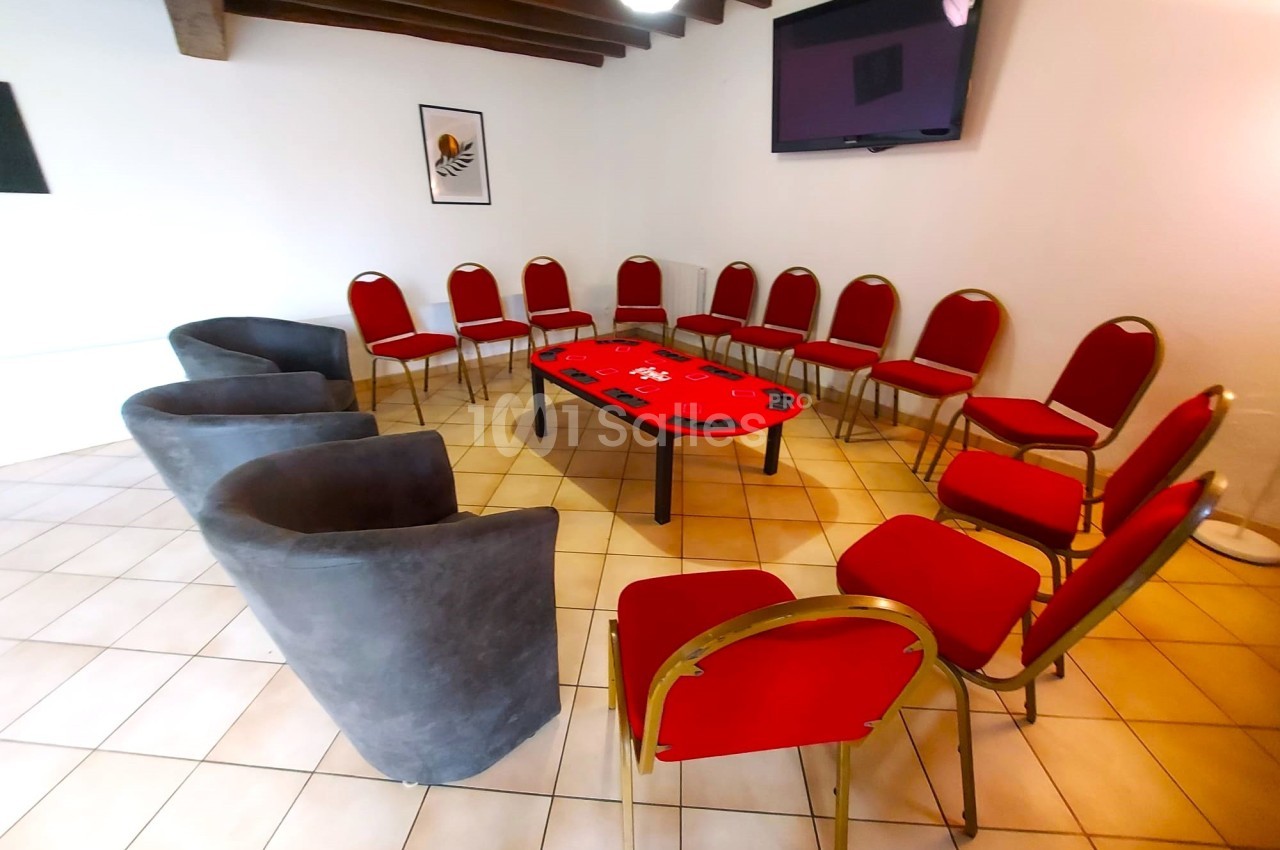 Salle de réunion avec chaises rouges et fauteuils gris disposés en cercle autour d'une table basse rouge.