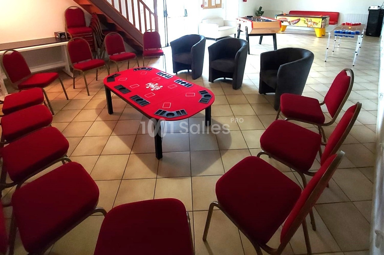 Salle aménagée avec des chaises rouges disposées autour d'une table de poker, dans un espace lumineux avec un baby-foot au…