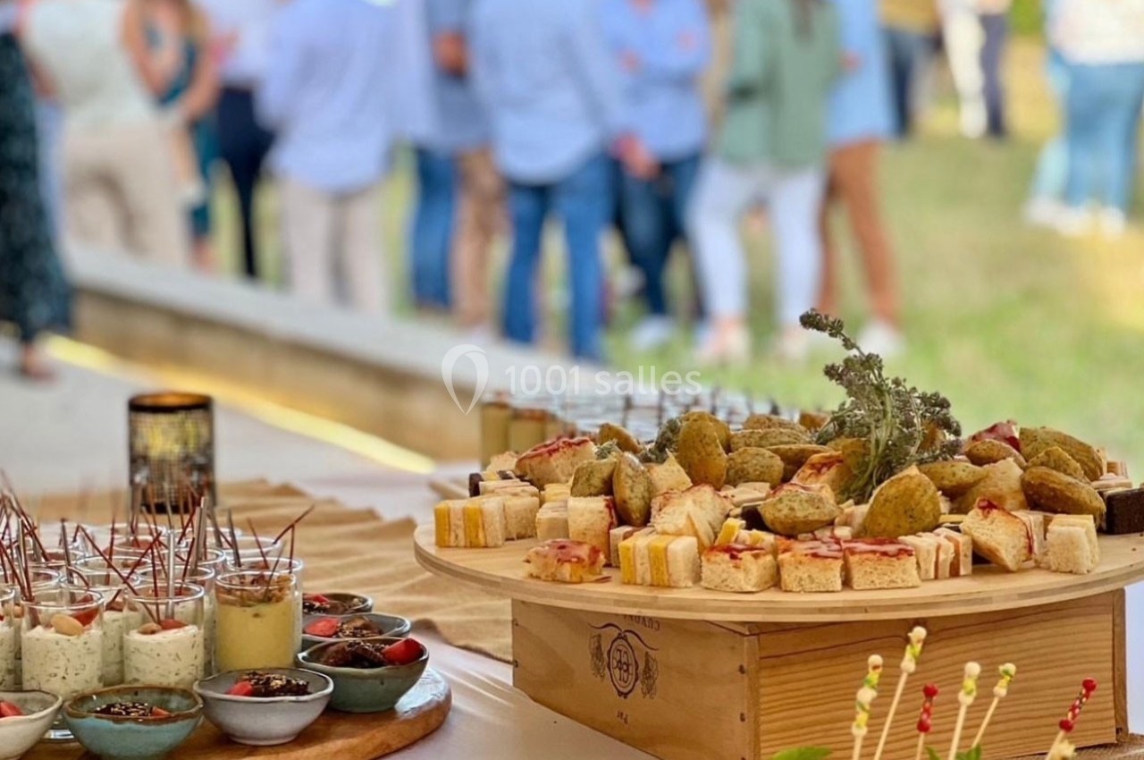 Plateau de bouchées apéritives variées disposées sur une table, avec un groupe de personnes flou en arrière-plan.