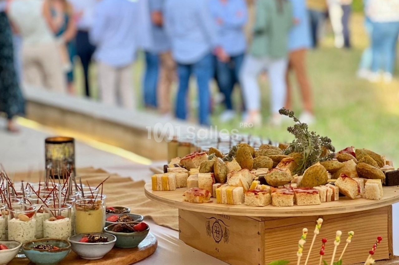 Plateau de bouchées apéritives variées disposées sur une table, avec un groupe de personnes flou en arrière-plan.