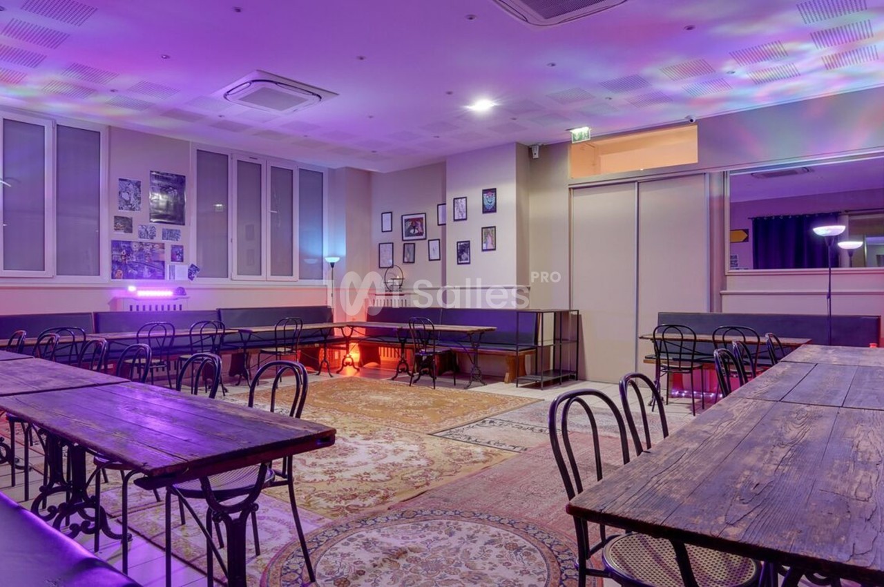 Salle lumineuse avec tables en bois, chaises en métal, murs décorés de cadres et éclairage coloré.