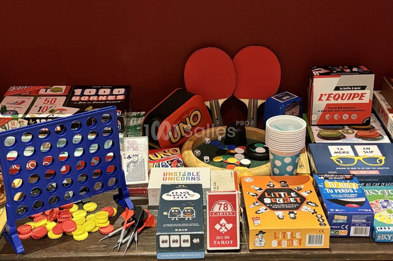 Jeux de société variés, accessoires de jeux de table et échiquier disposés sur une table devant un mur rouge.