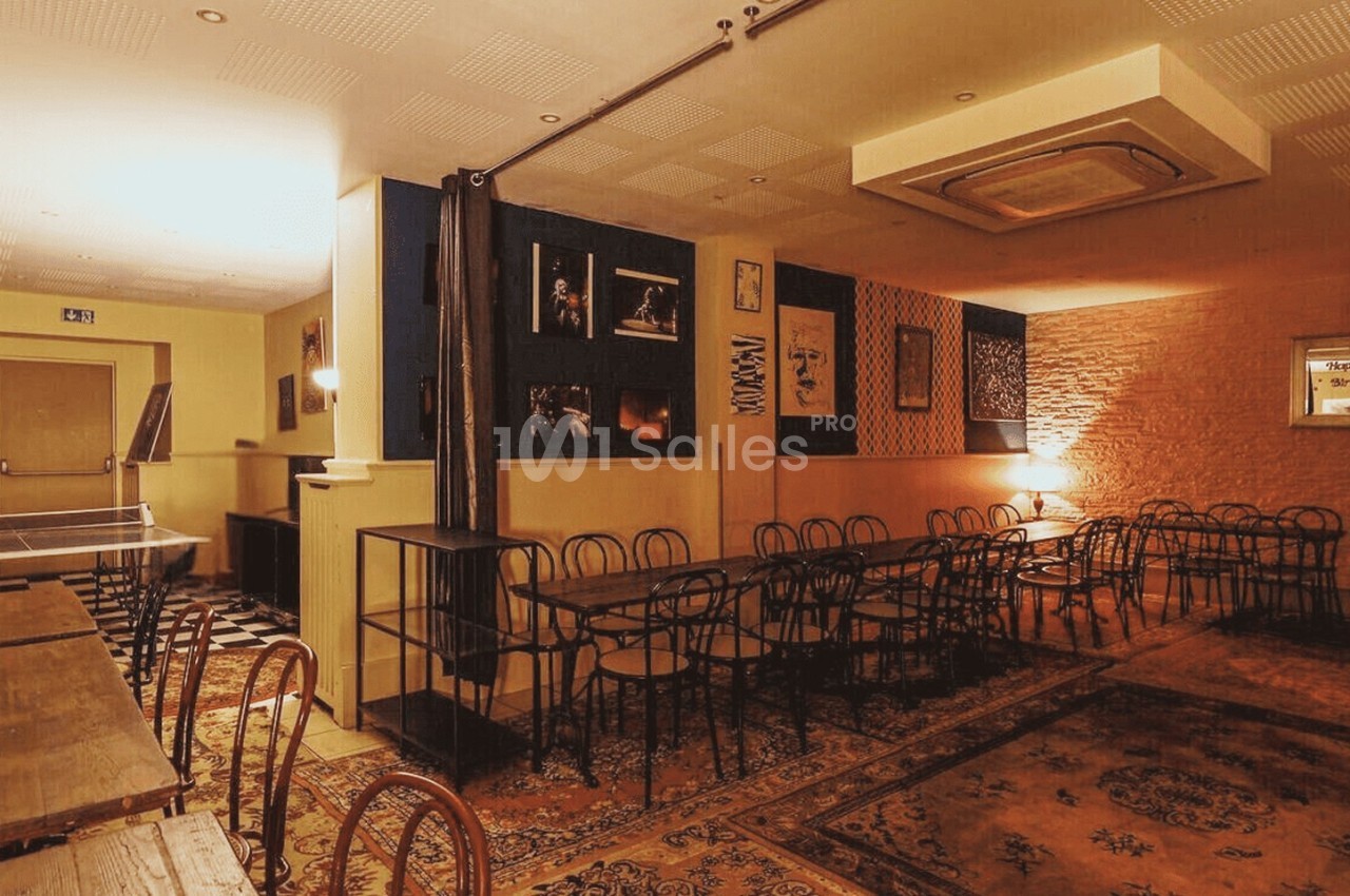 Salle chaleureuse avec tables en bois, chaises noires, décorations murales et éclairage tamisé.