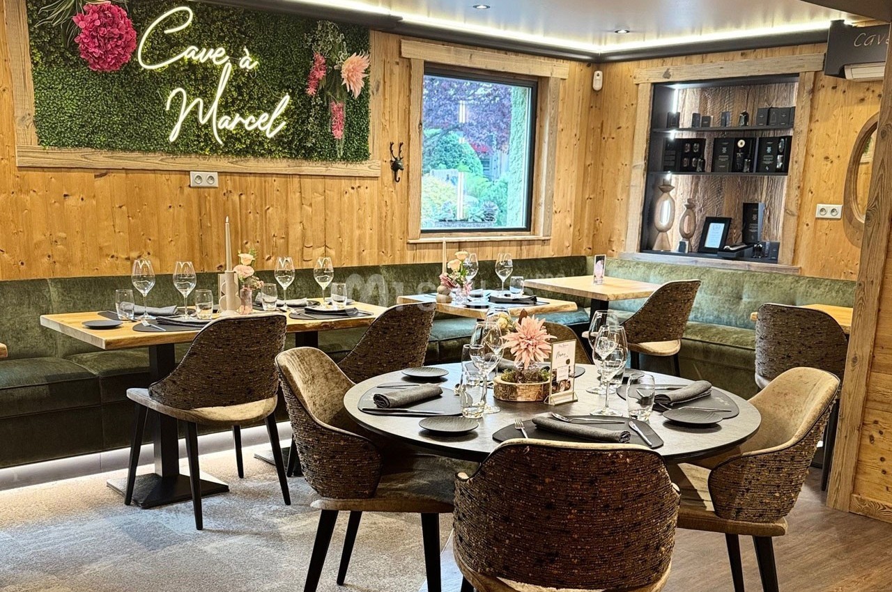 Salle de restaurant chaleureuse avec tables dressées, banquettes en bois et décoration murale végétale éclairée.