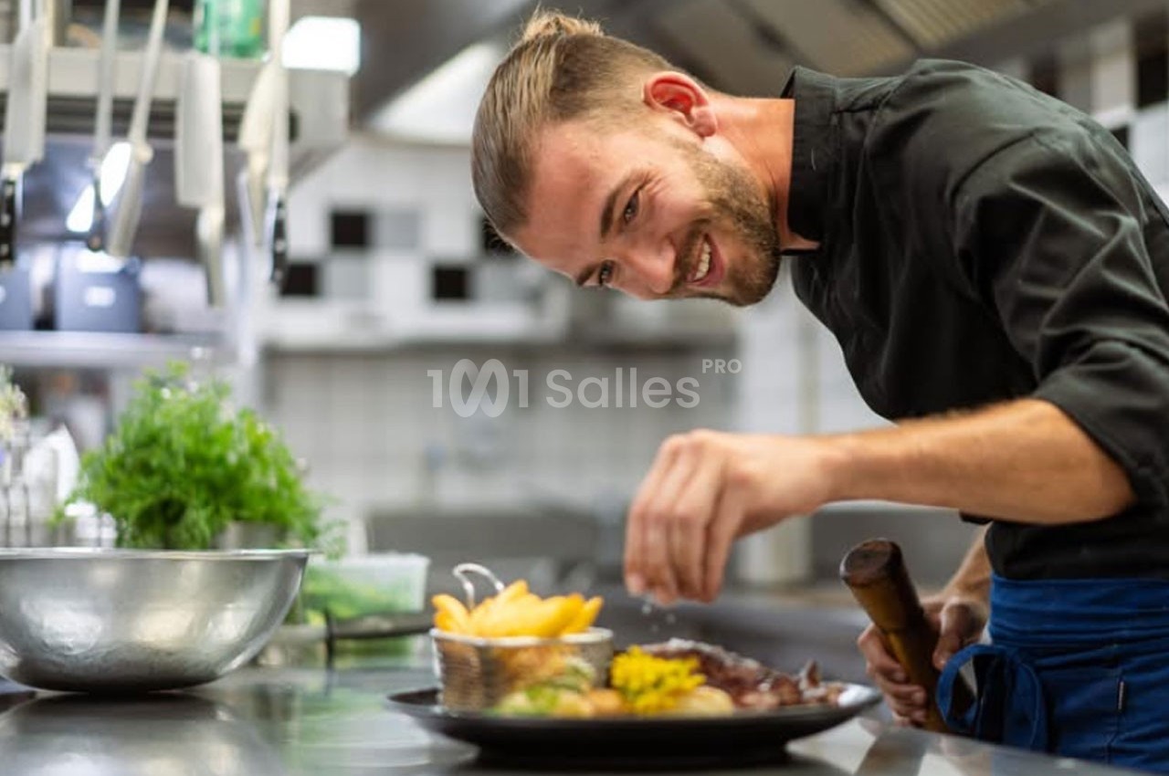 Un chef souriant dresse une assiette avec soin dans une cuisine professionnelle.