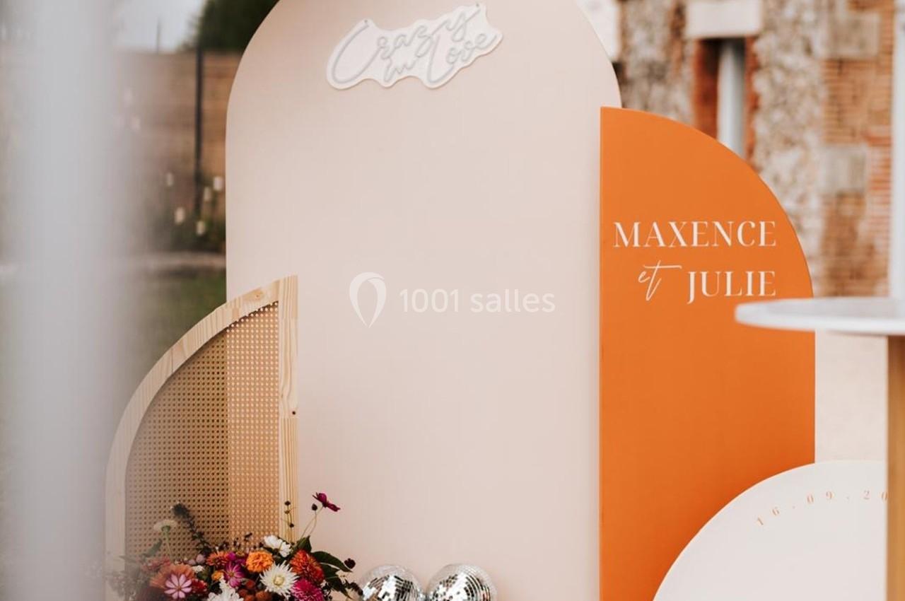 Décor de mariage avec panneaux colorés, fleurs, boules miroir et les prénoms ’Maxence et Julie’ inscrits.