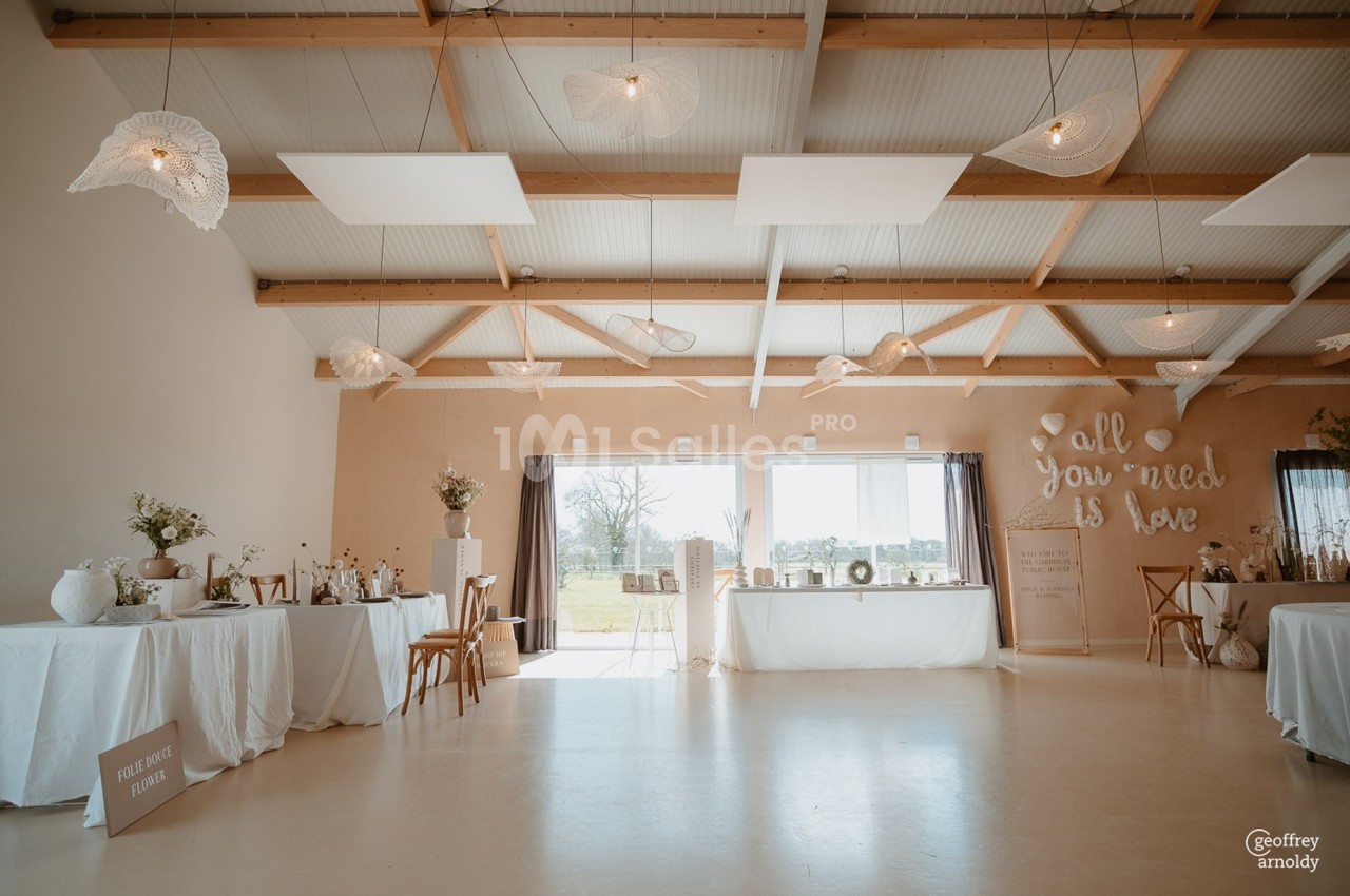 Salle lumineuse décorée pour un événement, avec des tables ornées de fleurs et des suspensions en forme de feuilles.