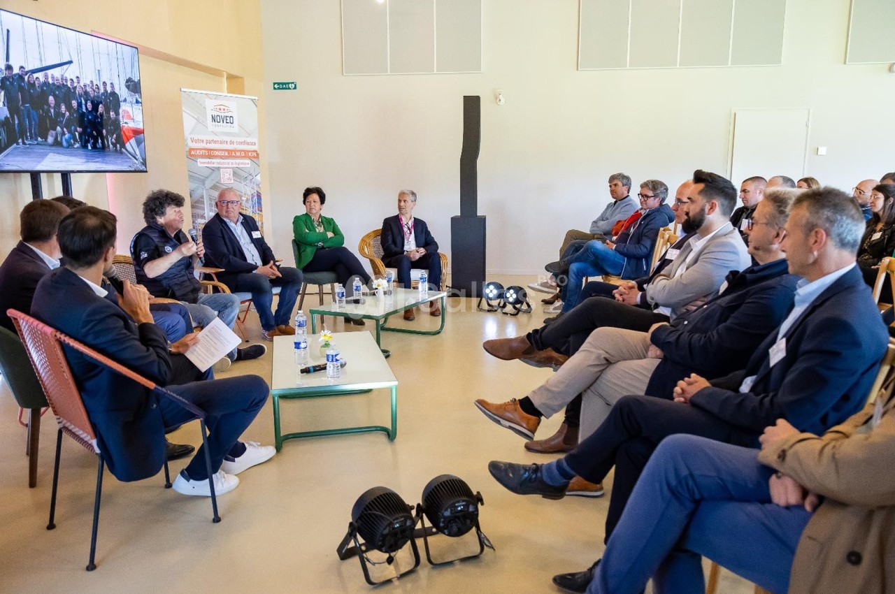 Un groupe de personnes assises en cercle participe à une discussion dans une salle lumineuse avec un écran en arrière-plan.