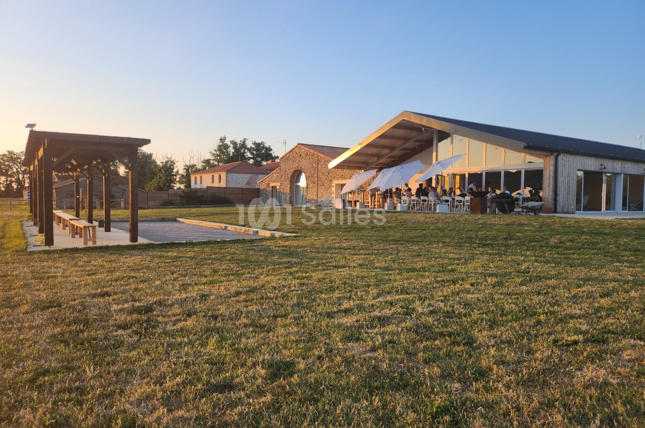 Bâtiment moderne avec terrasse ombragée, pergola en bois et pelouse au premier plan, sous un ciel dégagé.