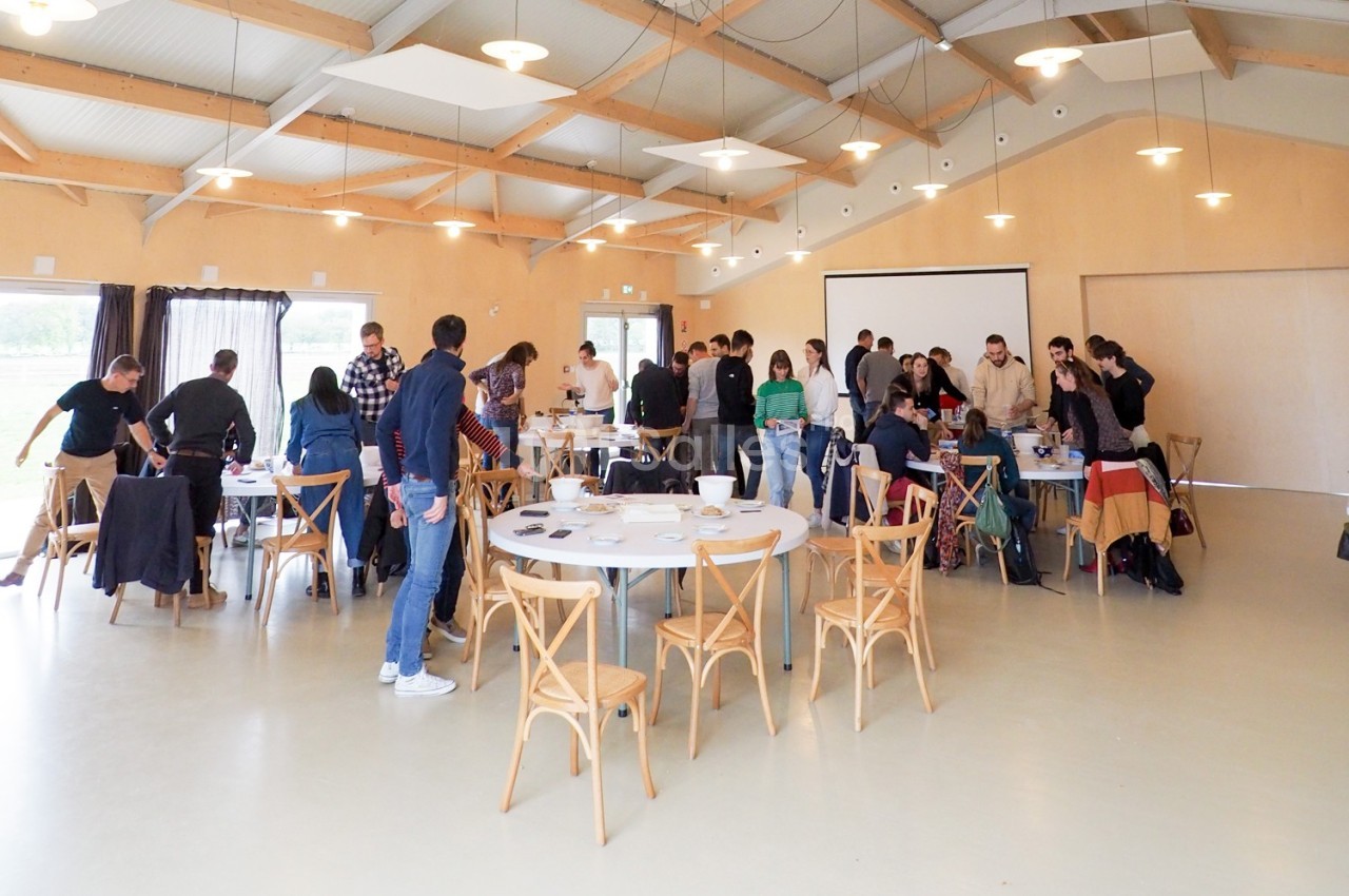 Des personnes discutent et travaillent en groupe autour de tables dans une grande salle lumineuse au style moderne.