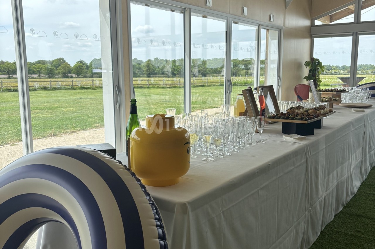 Table dressée avec des verres, des amuse-bouches et des décorations, près de grandes baies vitrées donnant sur un paysage…