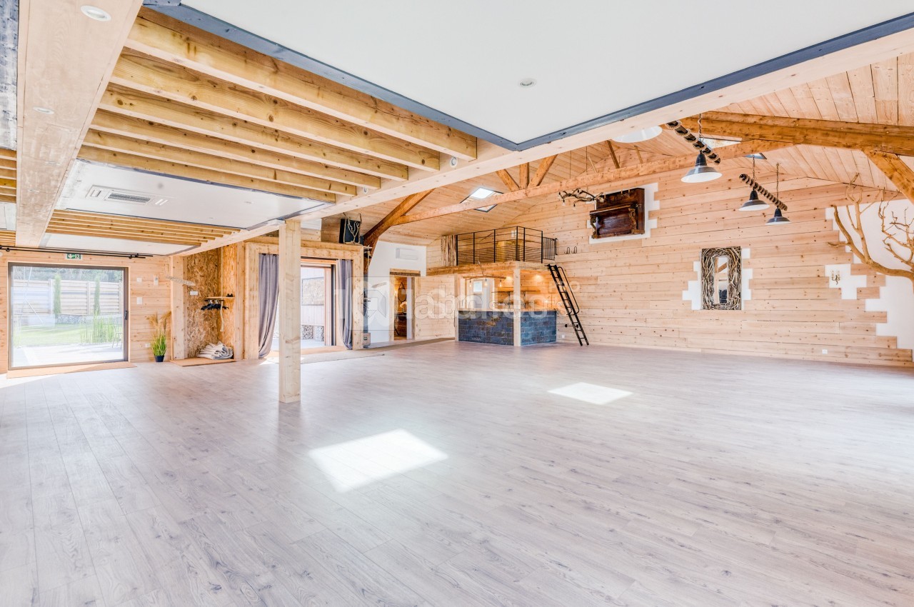 Salle spacieuse avec parquet clair, murs en bois, poutres apparentes et mezzanine avec escalier métallique.