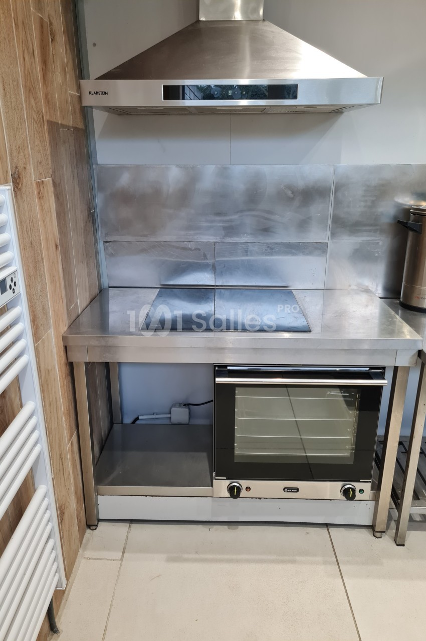 Cuisine équipée avec un four encastré, une plaque de cuisson et une hotte en acier inoxydable sur un plan de travail.