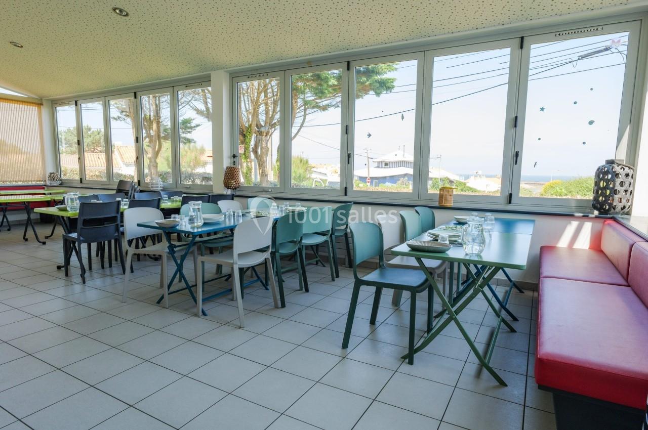 Salle de restaurant lumineuse avec des tables dressées, des chaises colorées et une vue sur l'extérieur à travers de grandes…
