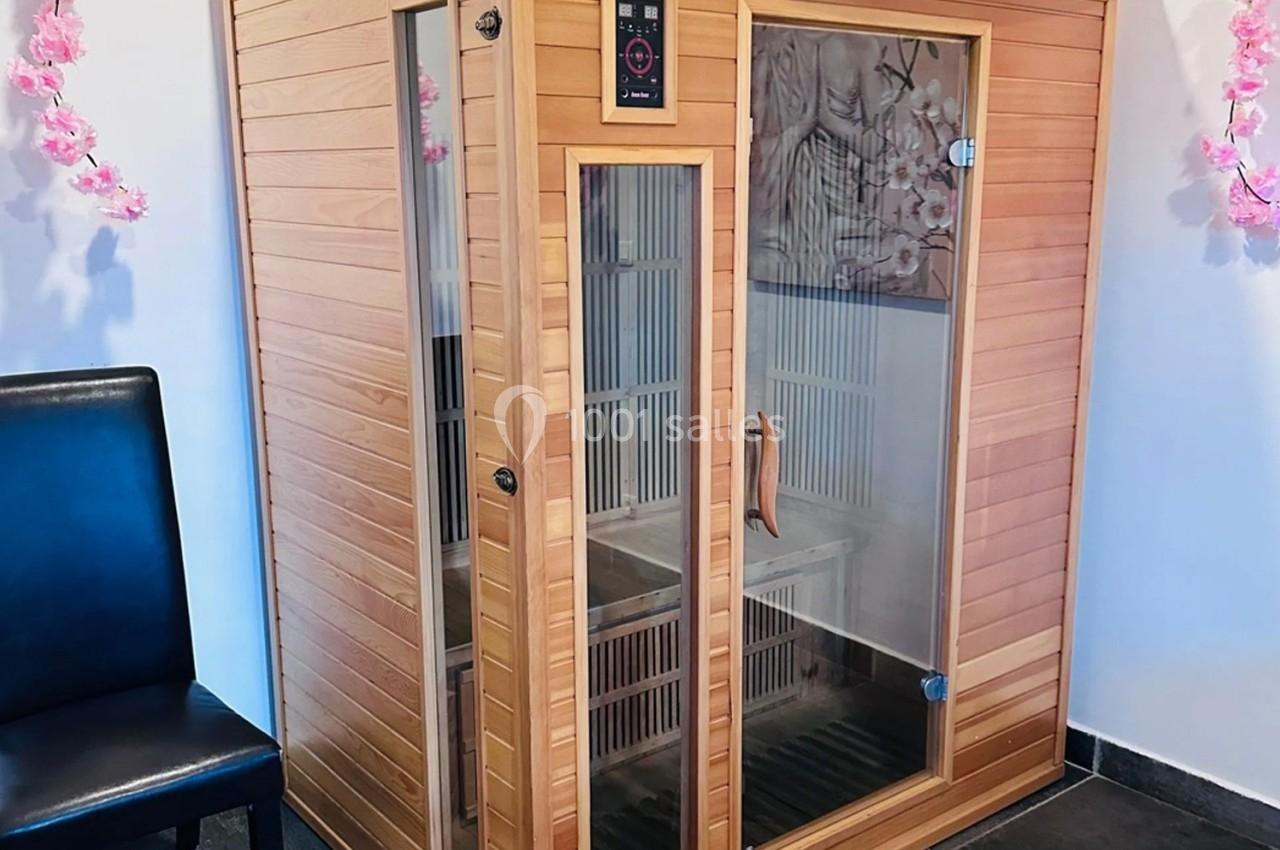 Cabine de sauna infrarouge en bois avec porte vitrée, entourée de décorations florales roses.