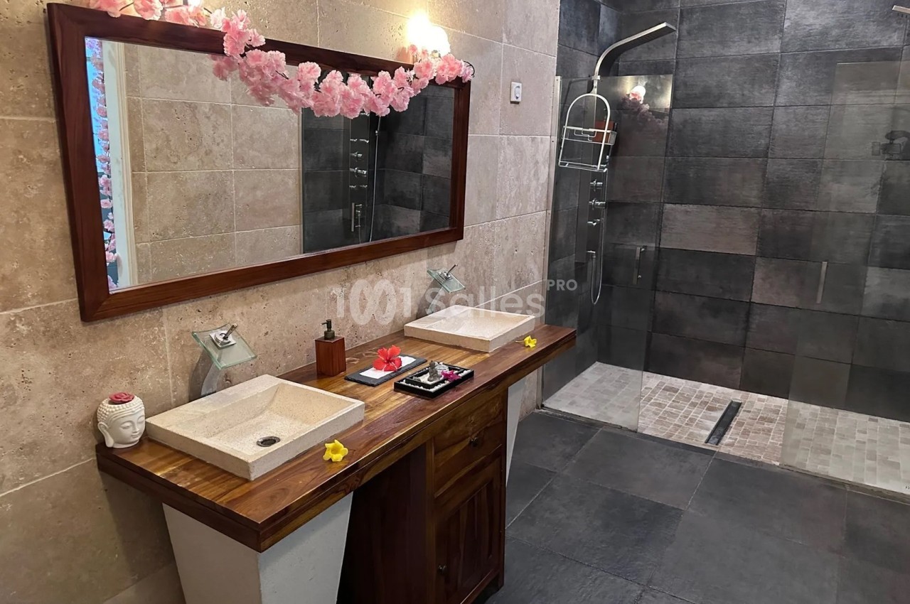 Salle de bain moderne avec double vasque en bois, grand miroir, douche à l'italienne et décoration florale.