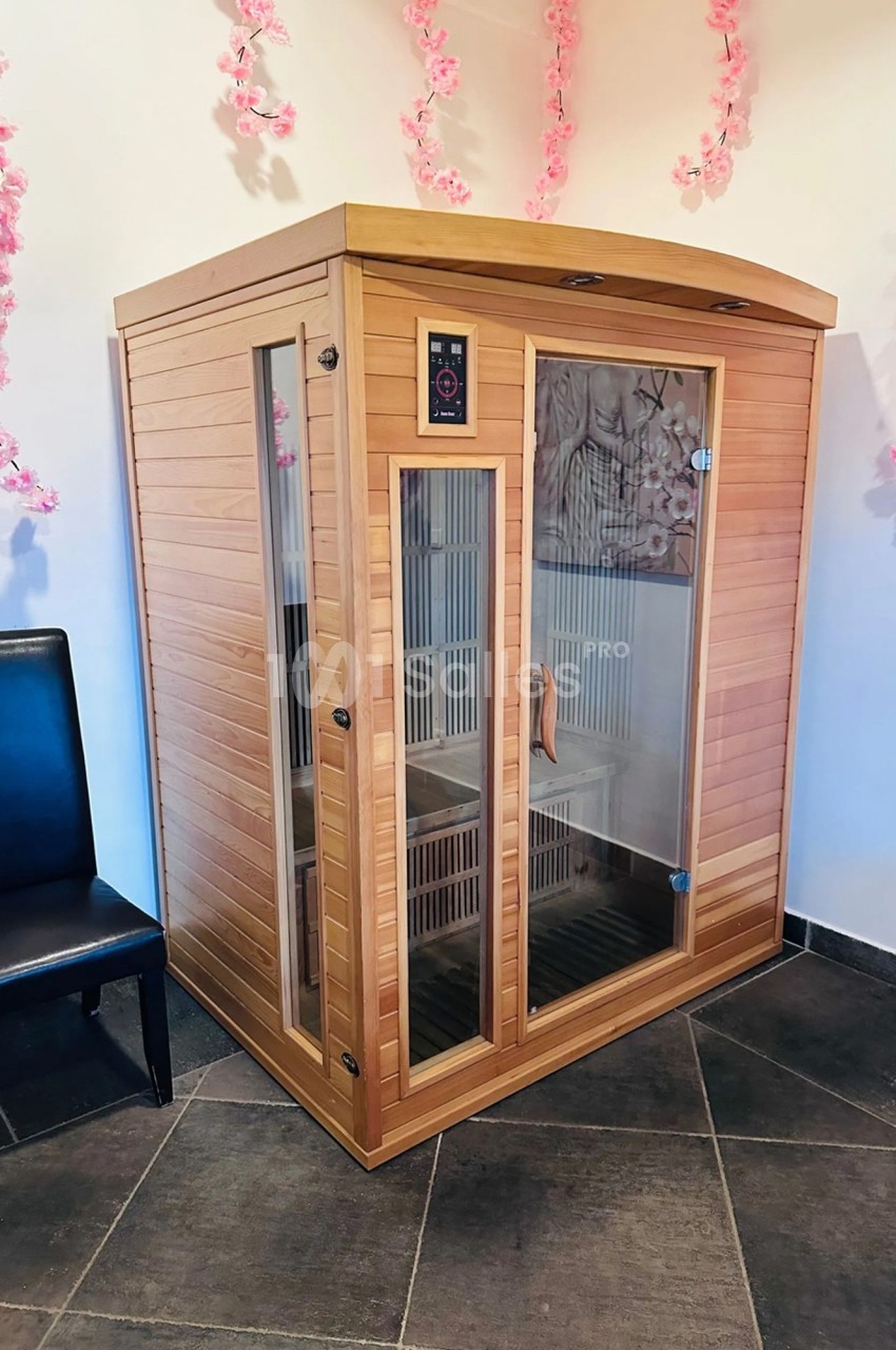 Cabine de sauna infrarouge en bois avec portes vitrées, entourée de décorations florales roses.