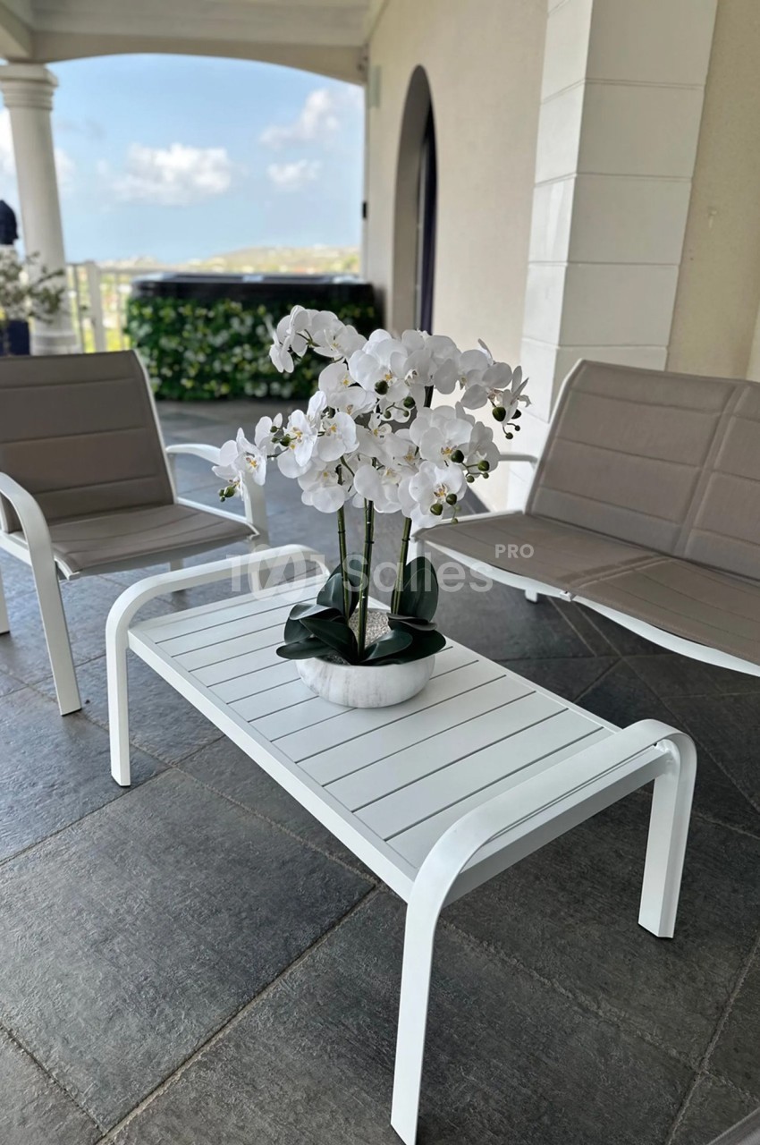 Table basse blanche avec une orchidée en pot, entourée de deux fauteuils beige sur une terrasse carrelée.
