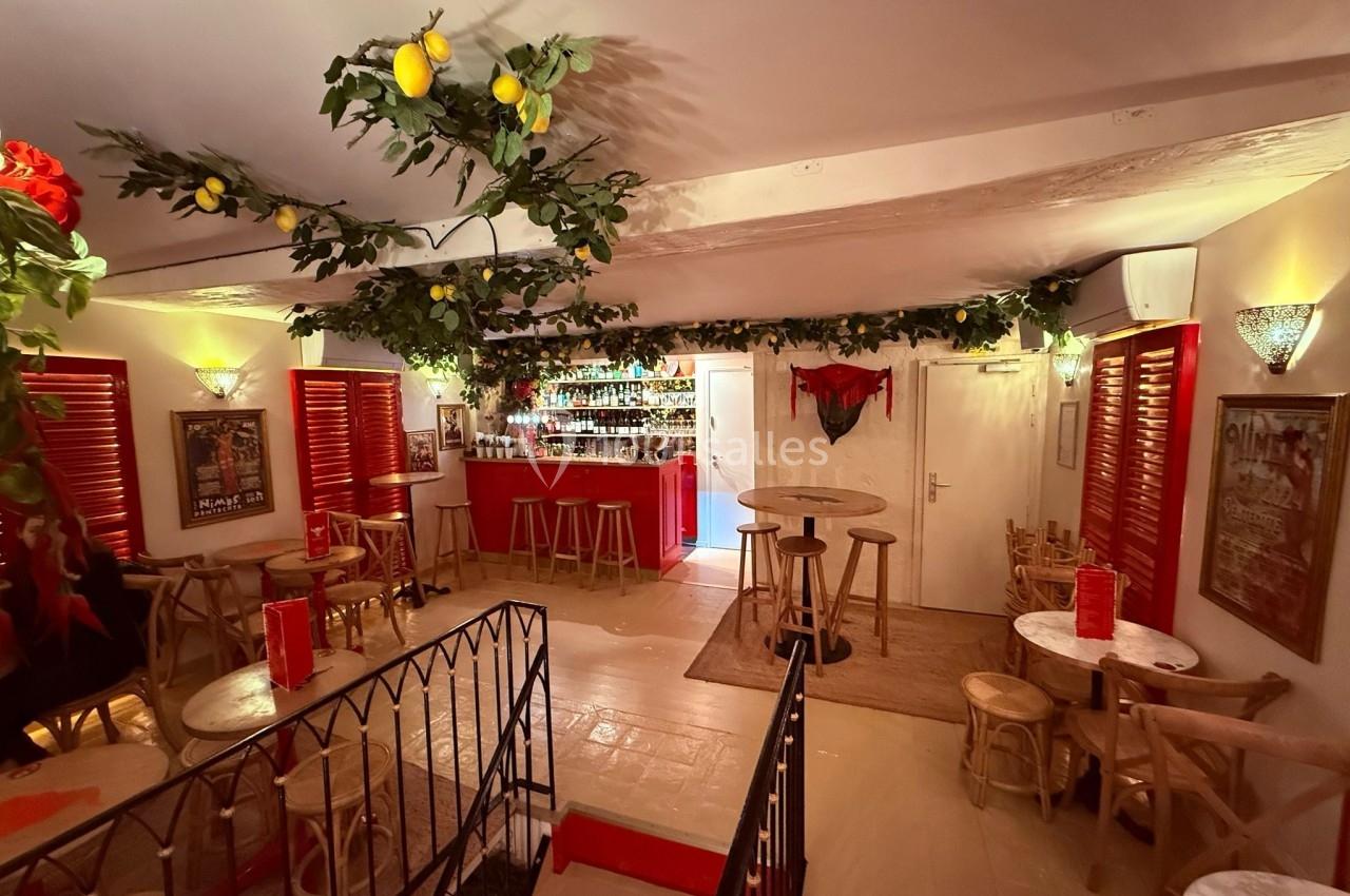 Salle de bar décorée de guirlandes végétales et de citrons, avec un comptoir rouge et des tables en bois clair.