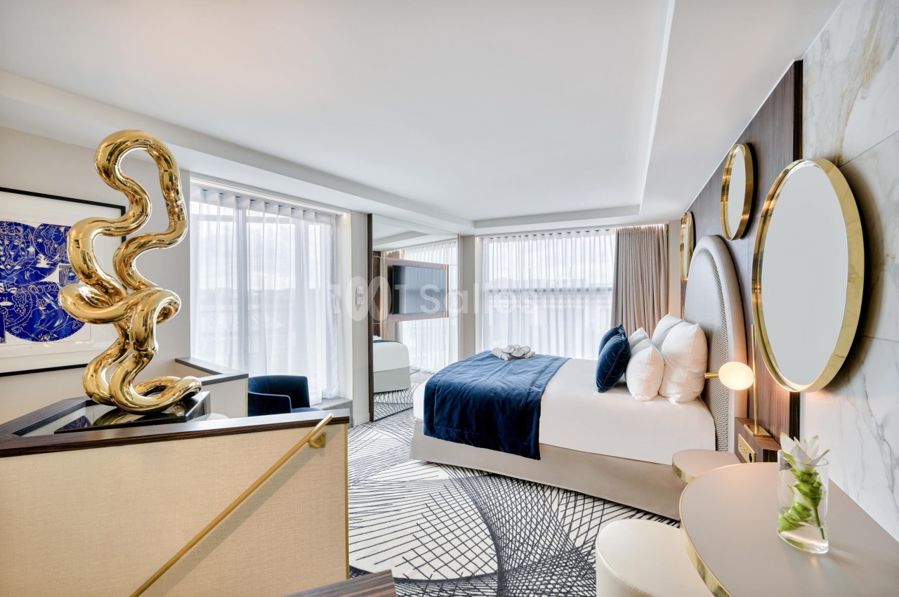 Chambre d'hôtel moderne avec lit double, décoration élégante, grandes fenêtres et sculpture dorée sur une table.