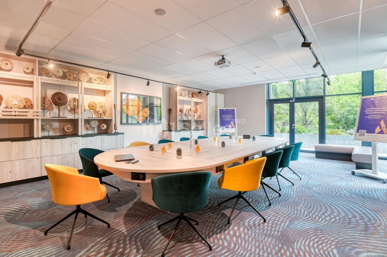 Salle de réunion lumineuse avec une grande table ovale, chaises colorées et étagères décorées en arrière-plan.