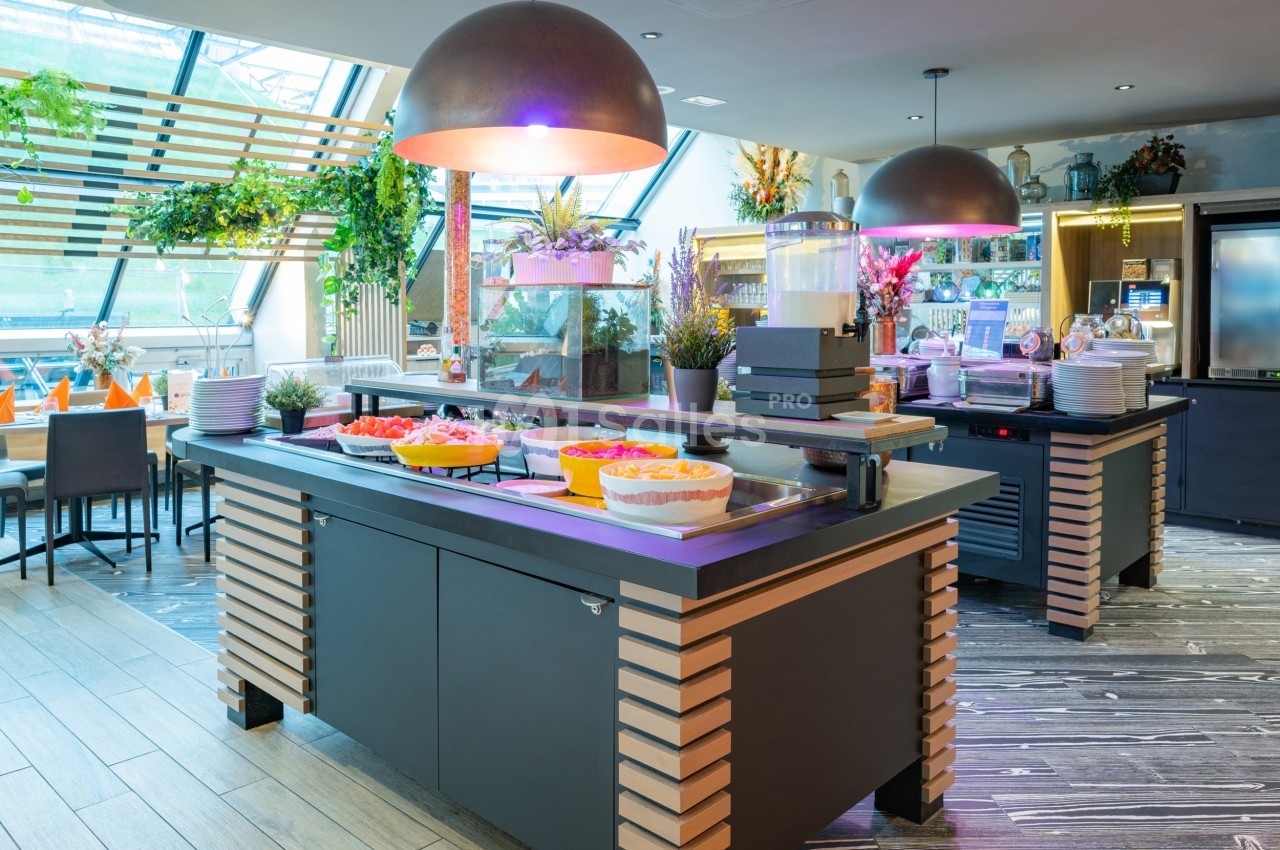 Buffet de restaurant avec plats variés, boissons et décoration végétale dans un espace lumineux et moderne.