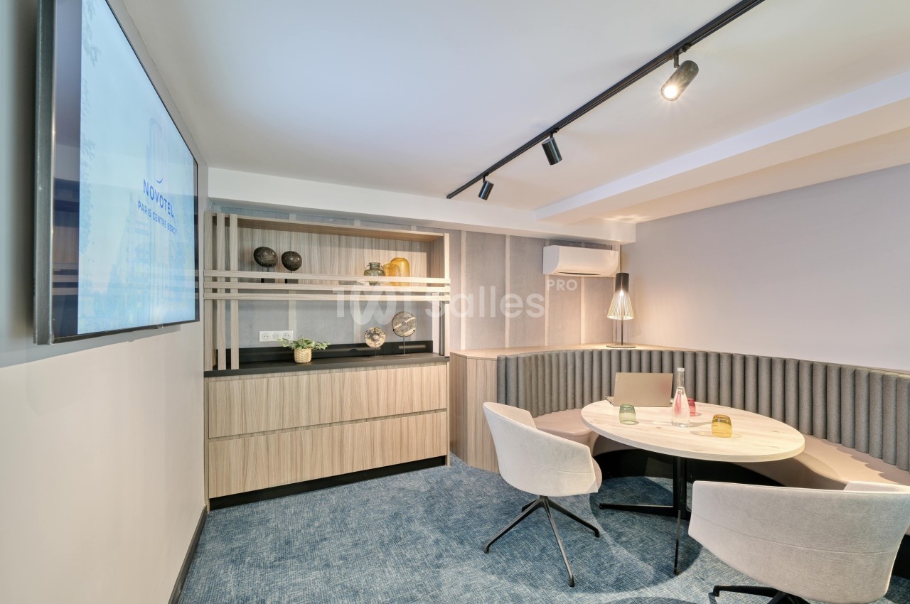 Salle de réunion moderne avec table ronde, chaises, étagères décoratives et écran mural.
