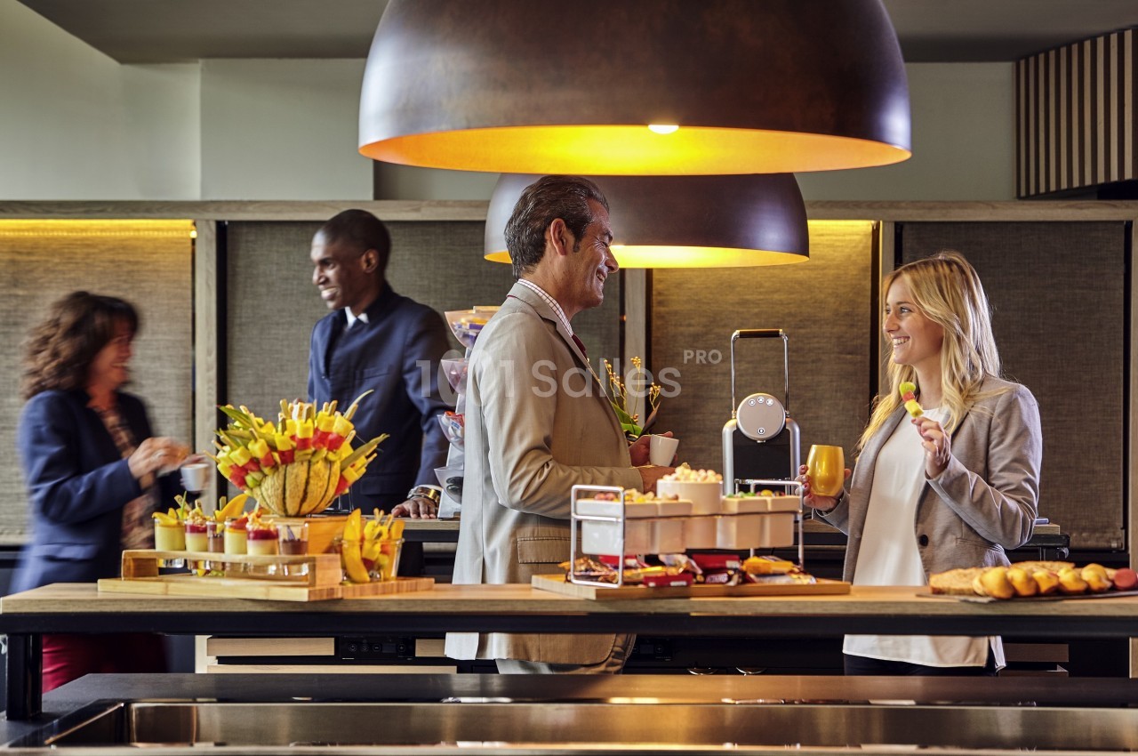 Des personnes discutent et se servent autour d'un buffet avec des boissons et des collations dans un cadre convivial.