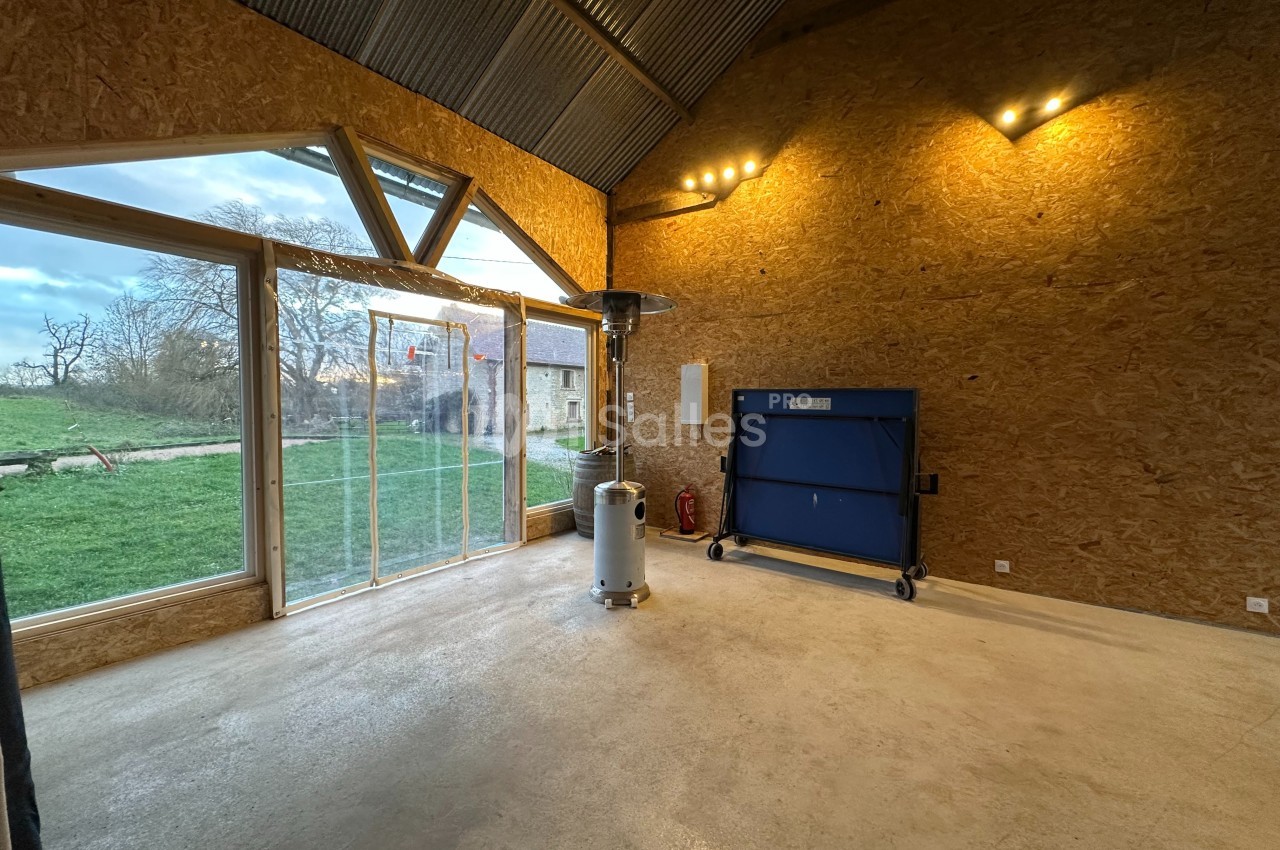 Intérieur d'une pièce avec grandes baies vitrées, murs en bois, un chauffage mobile et un conteneur bleu.