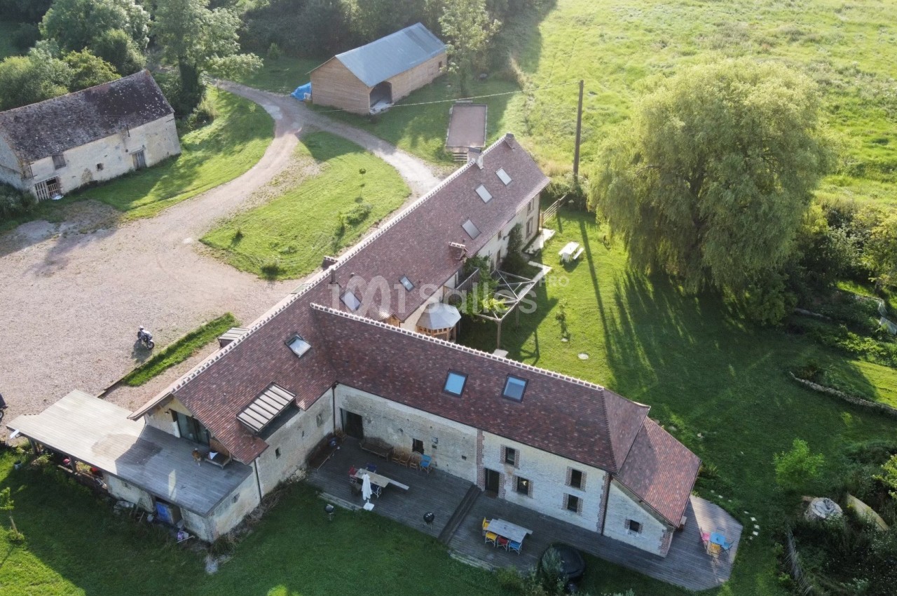 Vue aérienne d'une ferme en pierre avec toits en tuiles rouges, entourée de verdure et de bâtiments annexes.