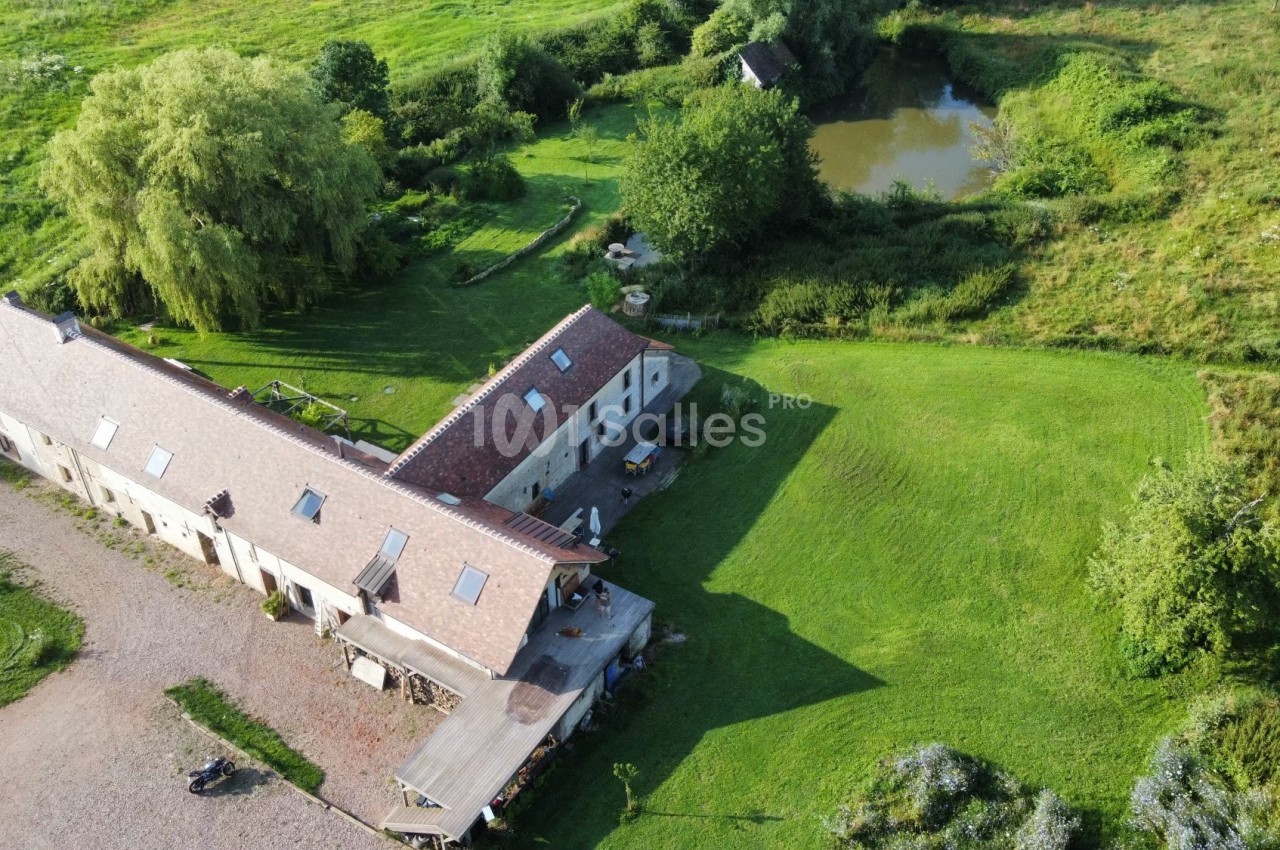 Vue aérienne d'une maison de campagne avec un grand jardin, un étang et des arbres environnants.