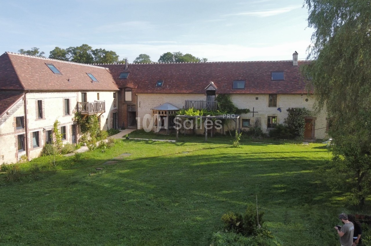 Bâtiment en pierre avec toit en tuiles rouges entouré d'une pelouse et d'arbres sous un ciel dégagé.