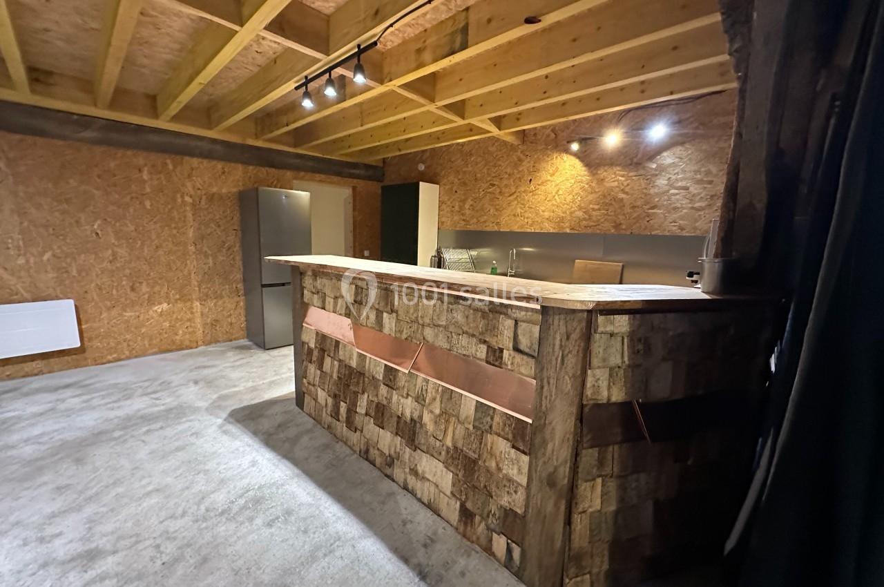 Cuisine moderne avec comptoir en bois brut, éclairage intégré, réfrigérateur gris et murs en panneaux OSB.