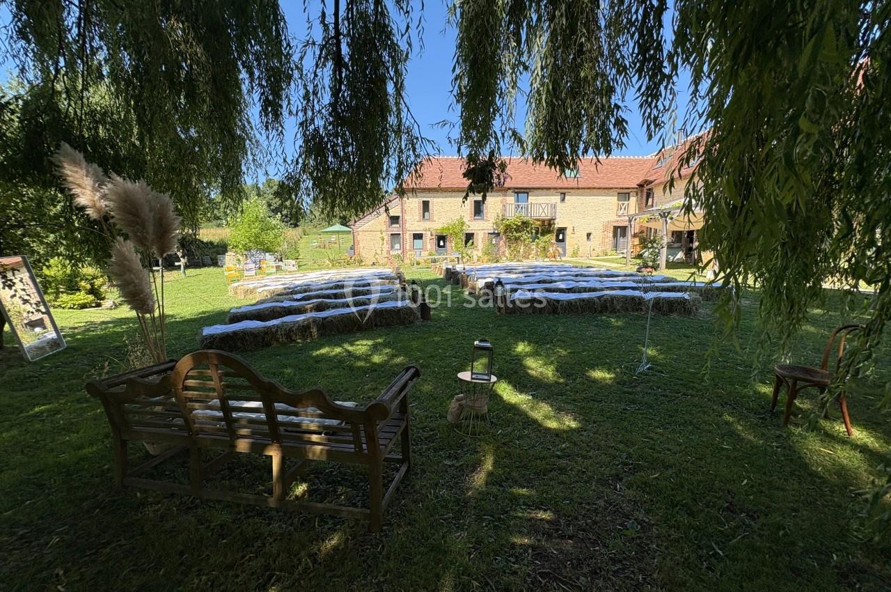 Chaises et bottes de foin disposées en extérieur pour une cérémonie, devant une maison en pierre sous un ciel dégagé.