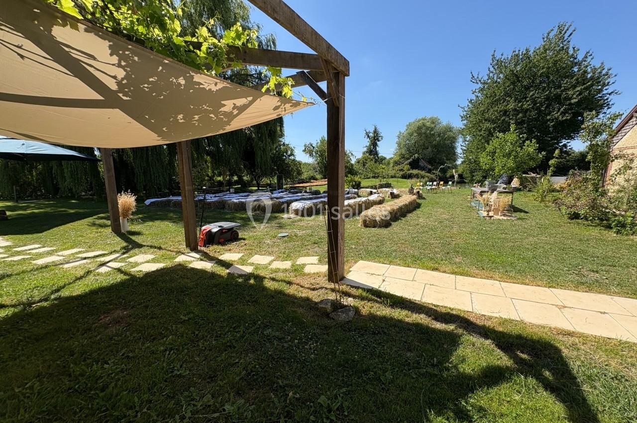 Jardin ensoleillé avec pergola, piscine hors-sol, bottes de paille et allée pavée sous un ciel bleu.