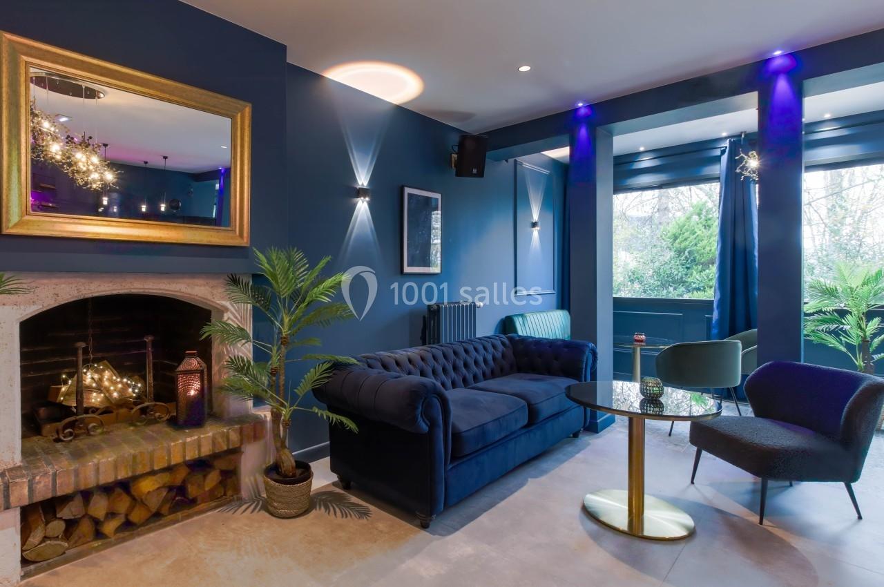 Salon élégant avec canapé bleu, cheminée décorative, plantes en pot et grande fenêtre laissant entrer la lumière naturelle.