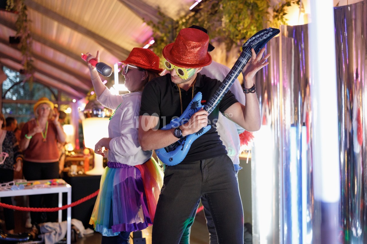 Deux personnes déguisées dansent et jouent avec des accessoires festifs dans un environnement lumineux et animé.