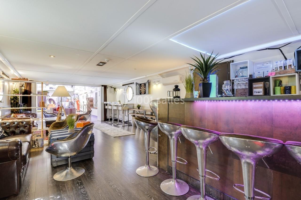 Intérieur d'un espace moderne avec un bar éclairé, des tabourets transparents et un coin salon confortable.