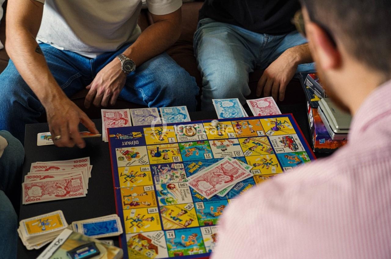Des personnes jouent à un jeu de société coloré avec des cartes et des billets sur une table.