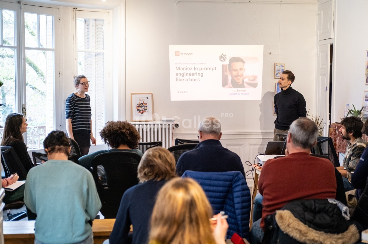 Un groupe de personnes assiste à une présentation dans une salle lumineuse avec un écran projetant des informations.