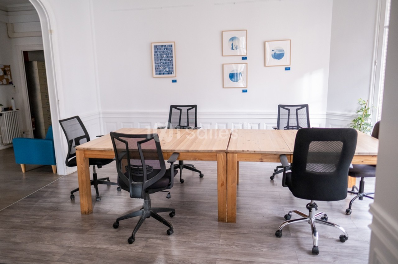 Salle de réunion lumineuse avec une grande table en bois, plusieurs chaises de bureau et des cadres au mur.
