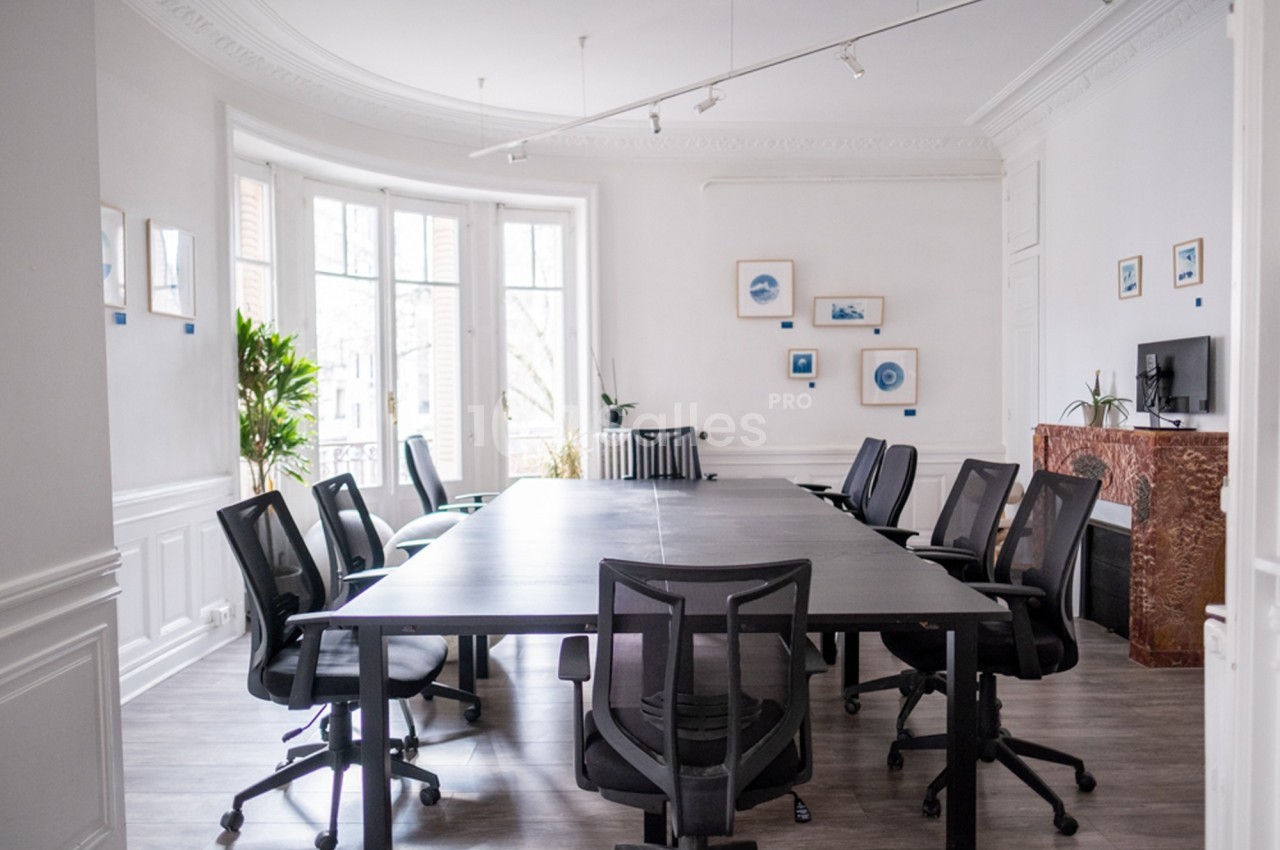 Salle de réunion lumineuse avec une grande table noire, des chaises de bureau et des cadres accrochés aux murs blancs.