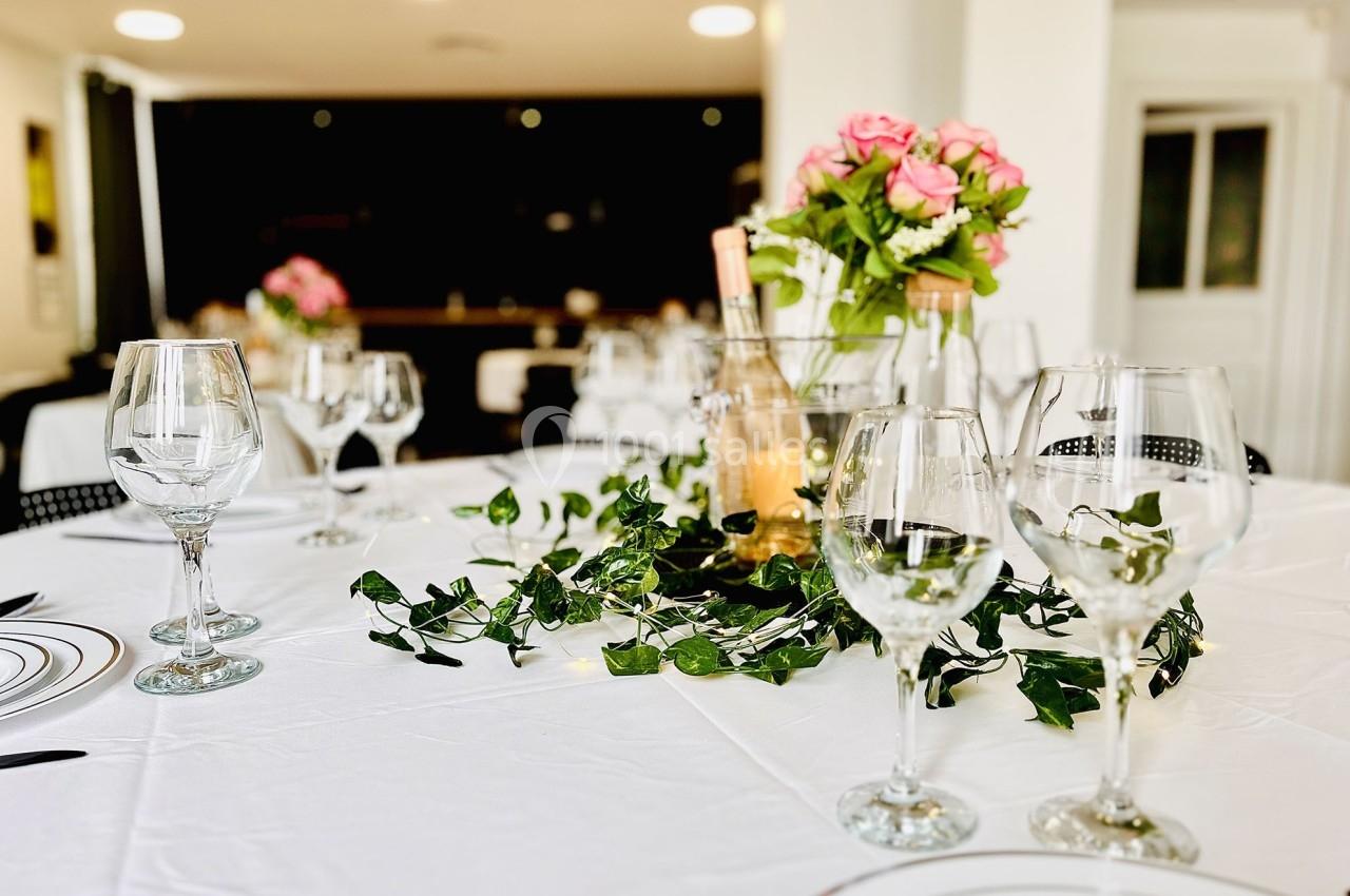 Table dressée avec une nappe blanche, verres, assiettes, centre de table fleuri et décorations végétales.