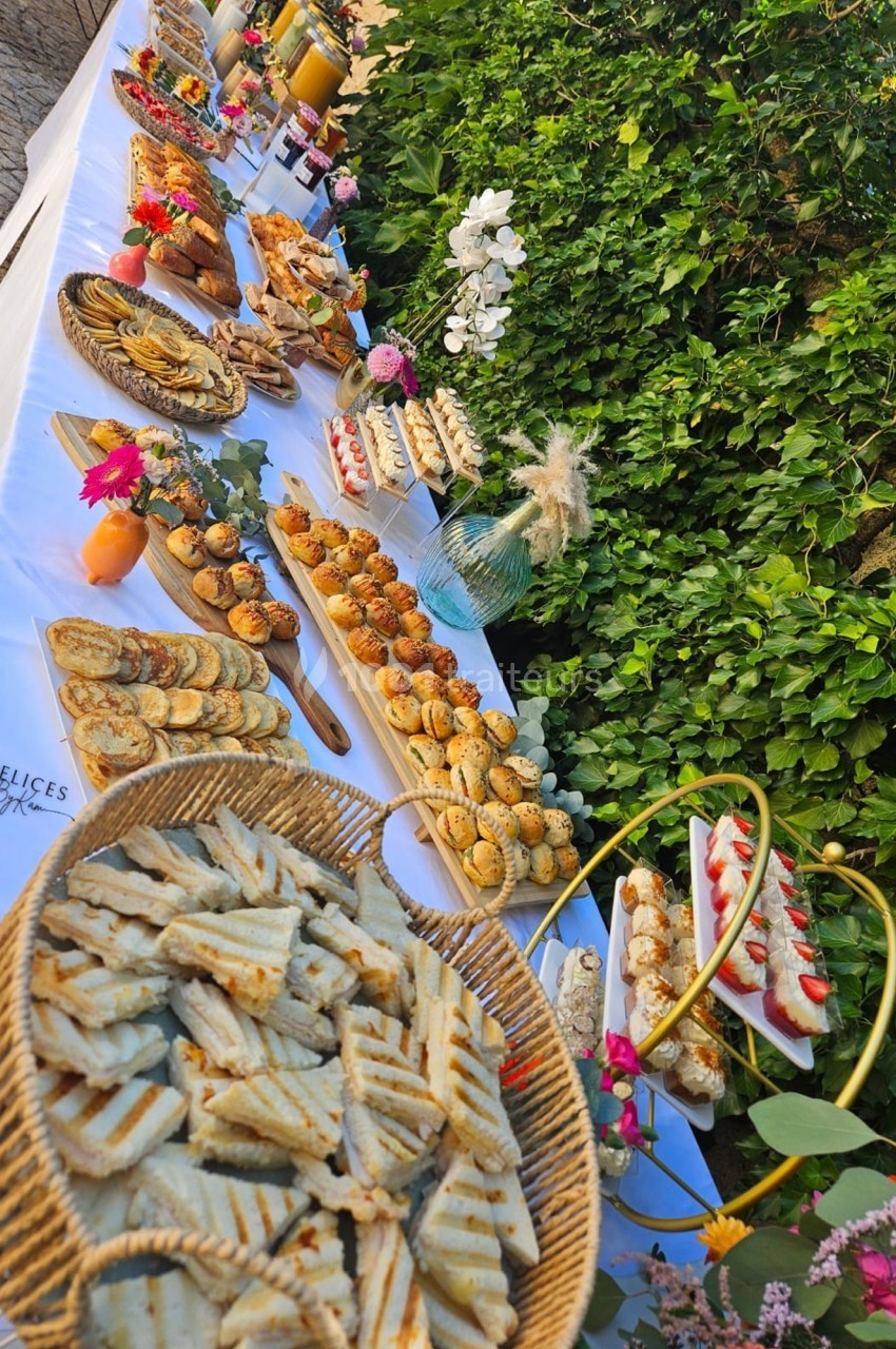 Buffet en extérieur avec divers plats, viennoiseries, fruits et boissons, disposés sur une table blanche décorée de fleurs.