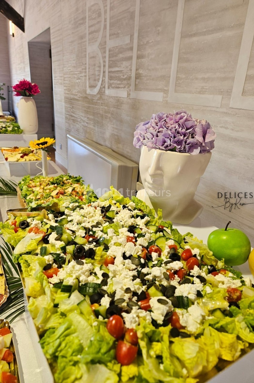 Buffet avec une grande salade composée de légumes frais, feta et olives, décoré de fruits et d'une tête vase fleurie.