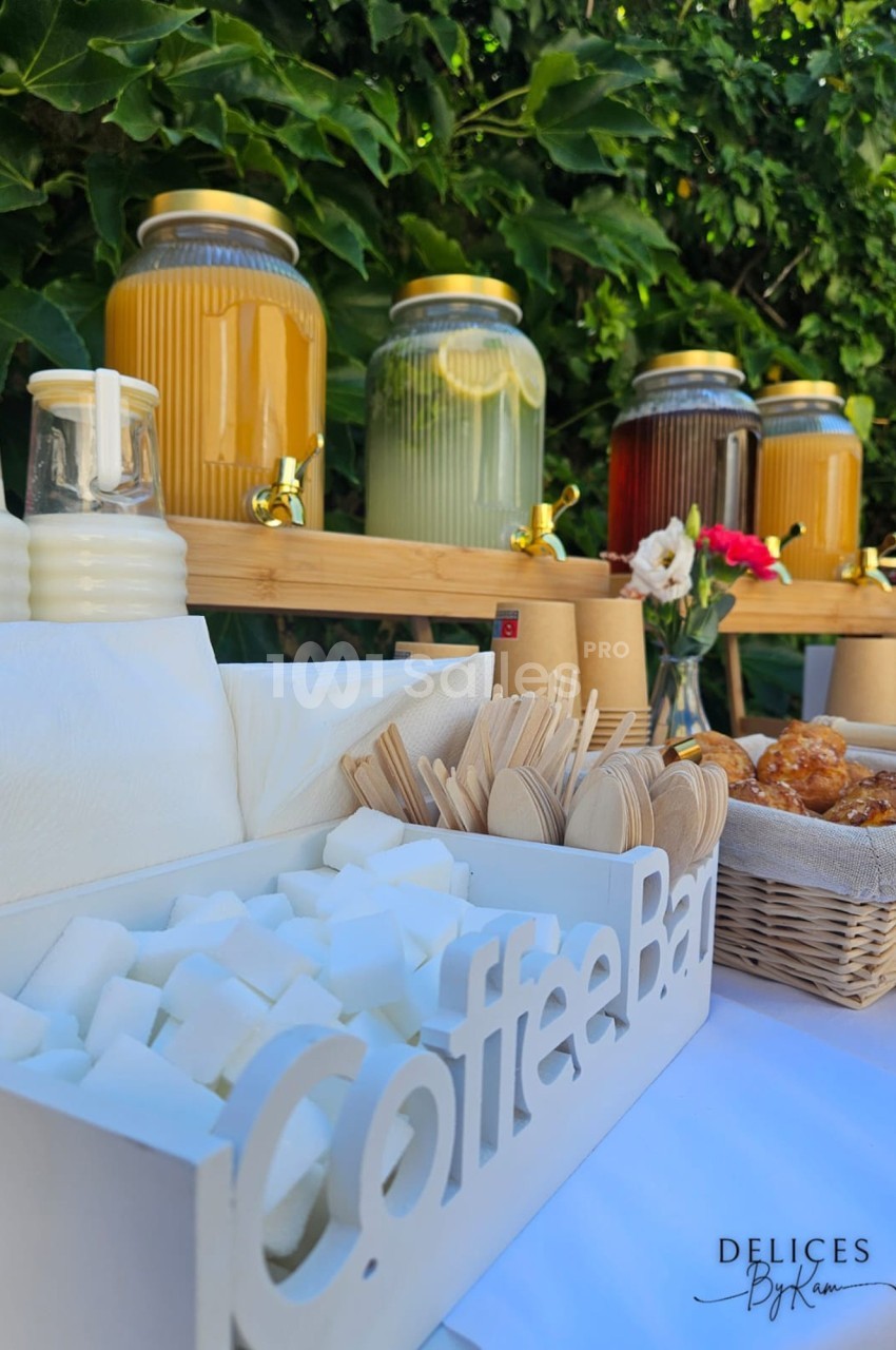 Buffet en plein air avec boissons en distributeurs, lait, sucre en morceaux, couverts en bois et viennoiseries.