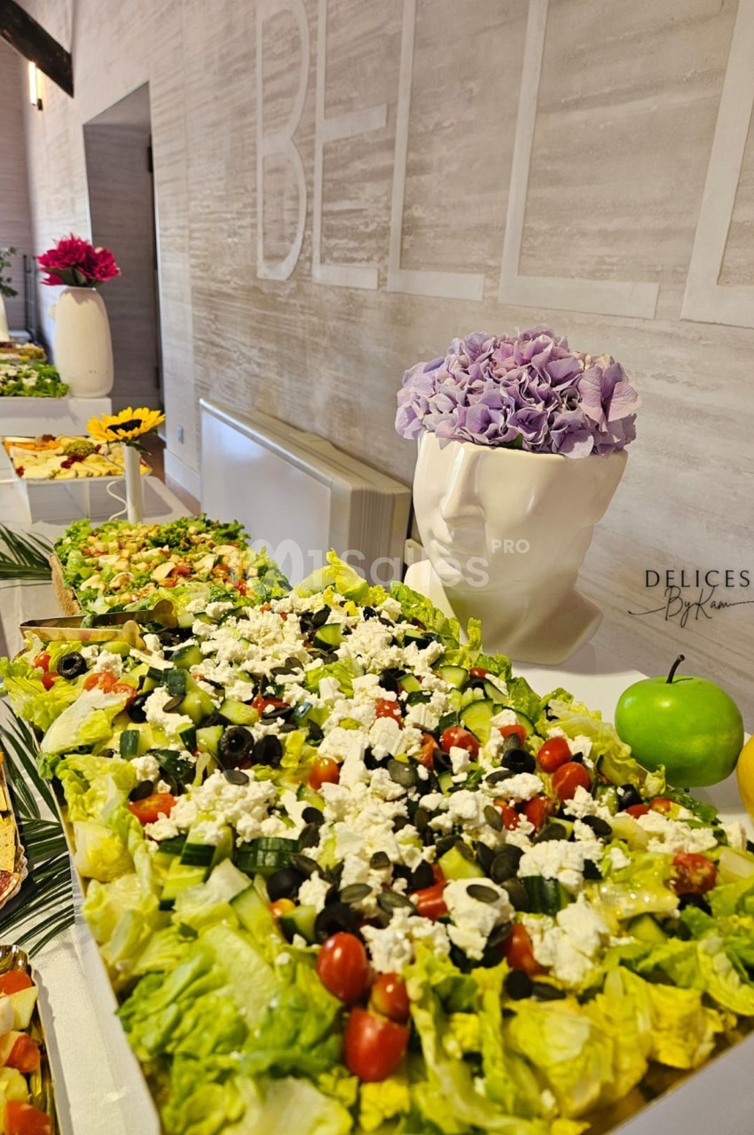 Buffet avec une grande salade composée de légumes frais, feta et olives, décoré de fruits et d'une tête vase fleurie.